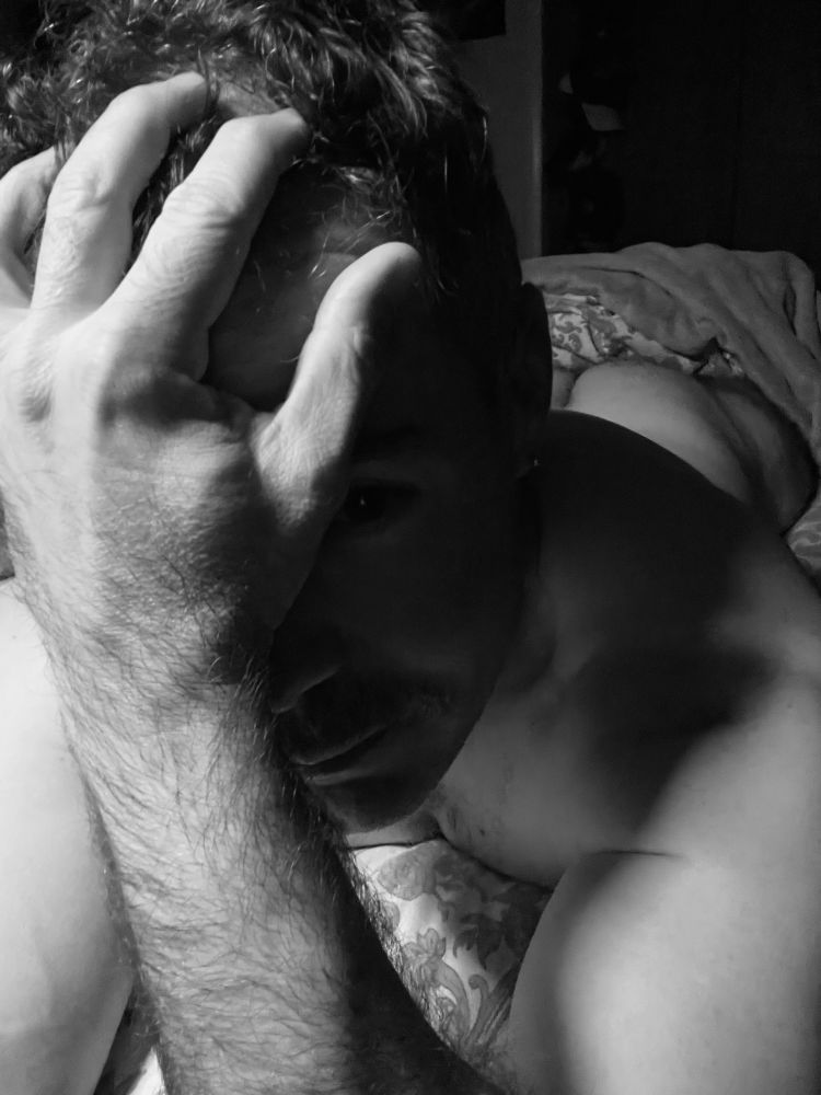 A black and white image of me, a white male, lying in bed in my stomach. Just a hint of butt is on display