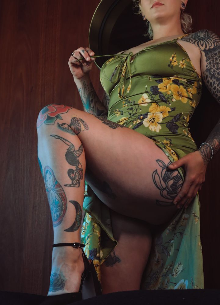 Frankie wears a green slip sundress against a dark wood panelled wall