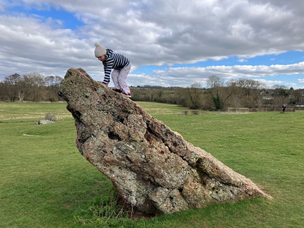 Small child wearing a woolly hat climbing a stone which is at a 45° angle.