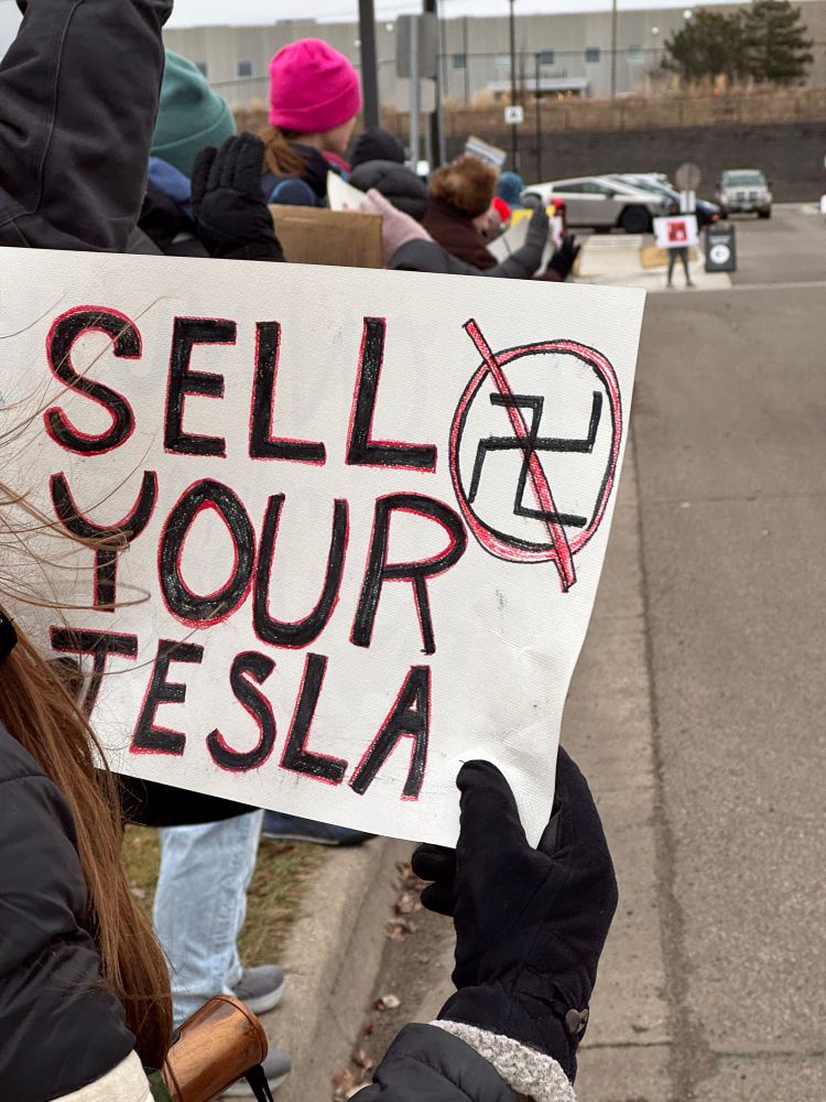 A person holds a sign that says “Sell your Tesla” with an anti-swastika graphic, at an Anti-Elon Musk protest outside a Tesla dealership in Golden Valley, Minnesota. 