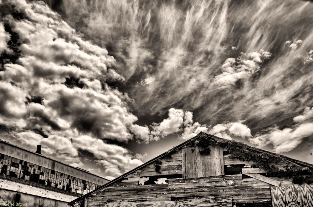 Two abandoned buildings in the foreground, with dramatic clouds overhead.  Black and white and toned.