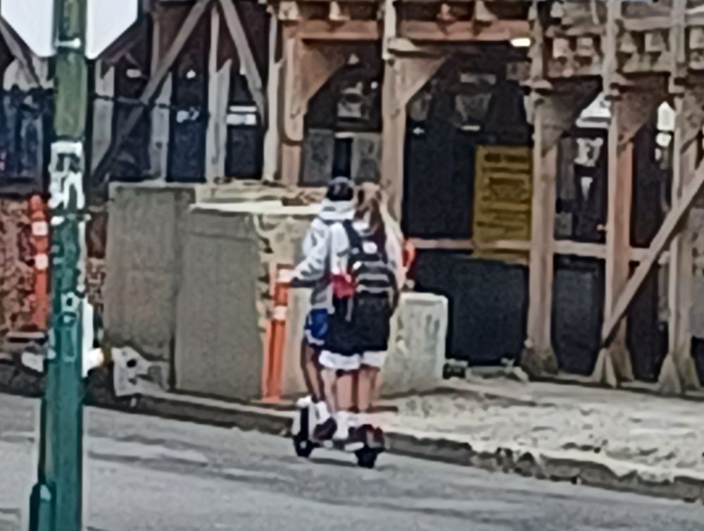 Two kids riding one Lime e-scoooter.