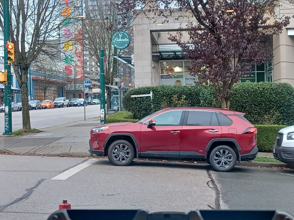 Red hatchback lets its nose hang into crosswalk so it can leave generous tire tread width between itself and service van behind it.