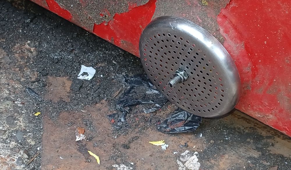 Showing steel sieve cap fastened over dumpster drain hole.