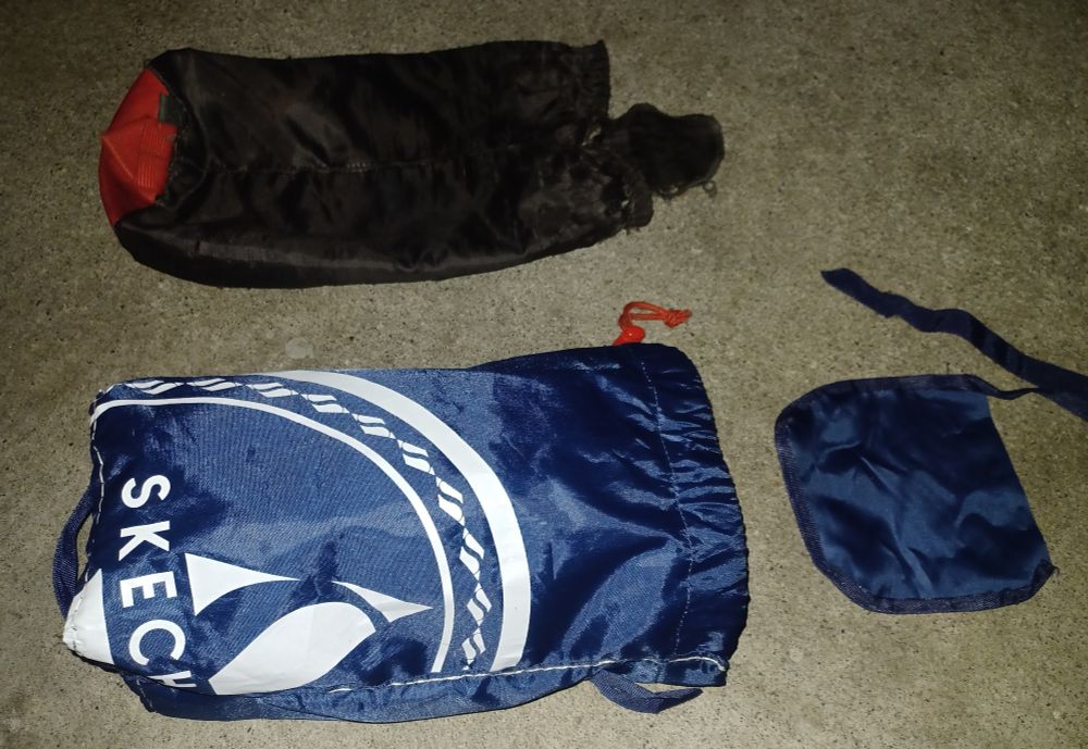 Original red and black nylon stuff sack - much worse for wear - above the heavier-weight blue nylon replacement I've almost finished making. Last unconnected piece is beside the new sack. It is an over-flap that fills any hole exposing the fleece liner after the sack's drawstring is pulled tight. New bag's flap is much larger than the original sack's 