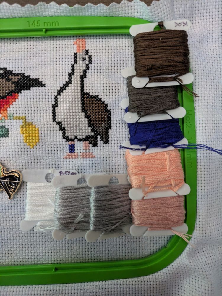 A cross stitch piece featuring a Laysan Albatross with a few thread bobbins framing it.