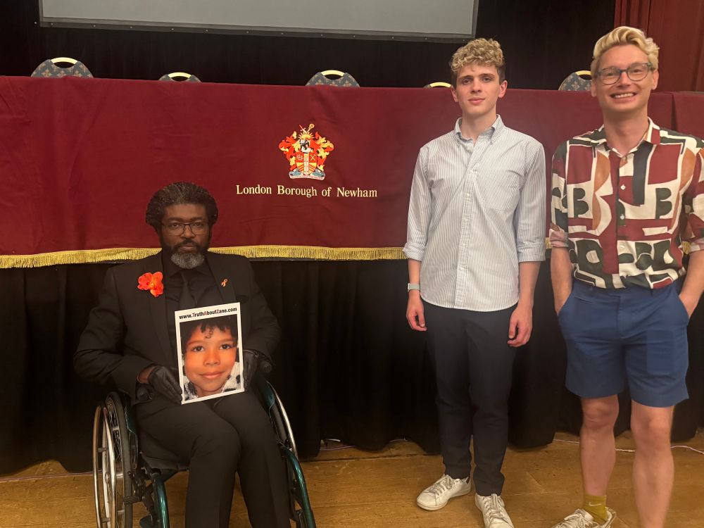 Photo of Kye, Nate and Danny in front of a London Borough of Newham crest. Kye is holding a photo of Zane with a “TruthAboutZane.com” URL.