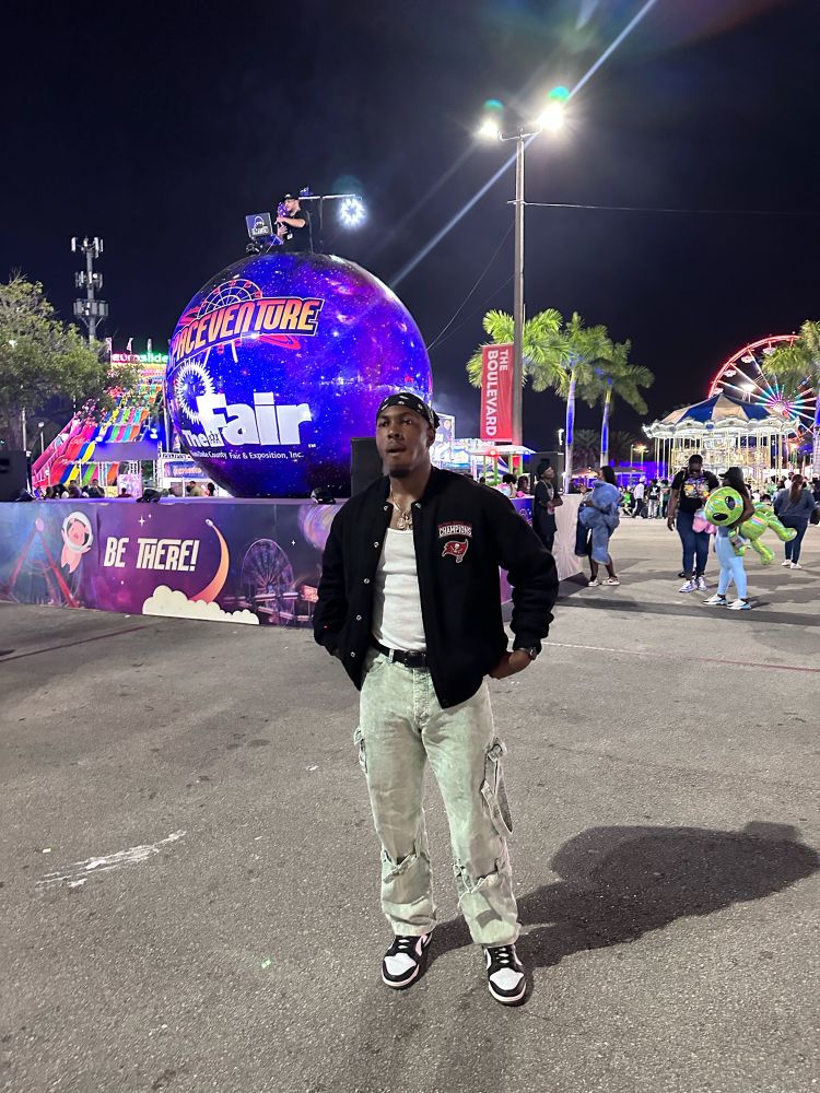 A Beautiful Black Man stands confidently at a vibrant fairground, surrounded by a diverse crowd. His genuine enjoyment of the event exemplifies the spirit of community and connection. Join him in celebrating life’s moments and creating lasting memories together. 