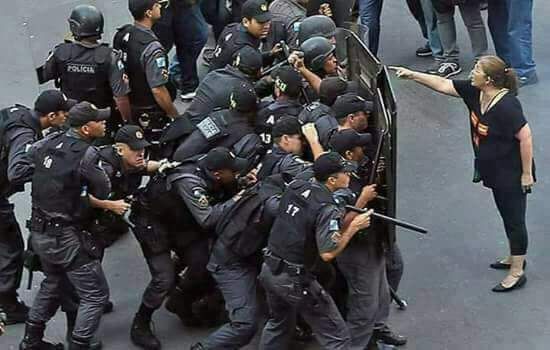 Professora enfrenta um grupo de policiais que se escondem atrás de escudos.