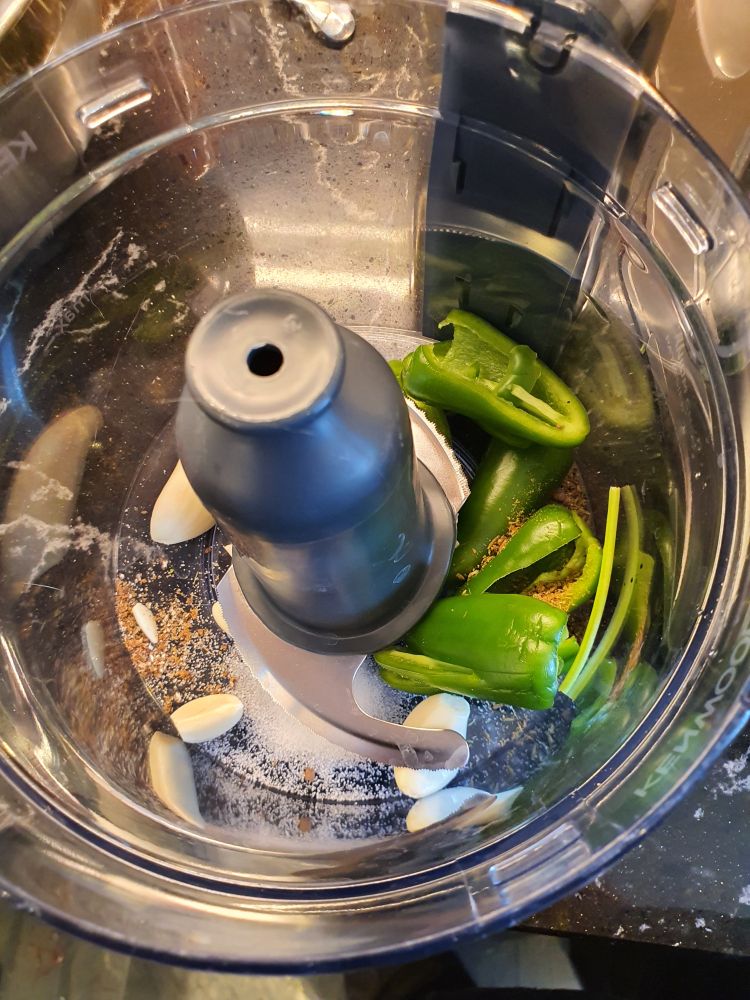 a photo of green chillies and garlic cloves and some spices in a blender