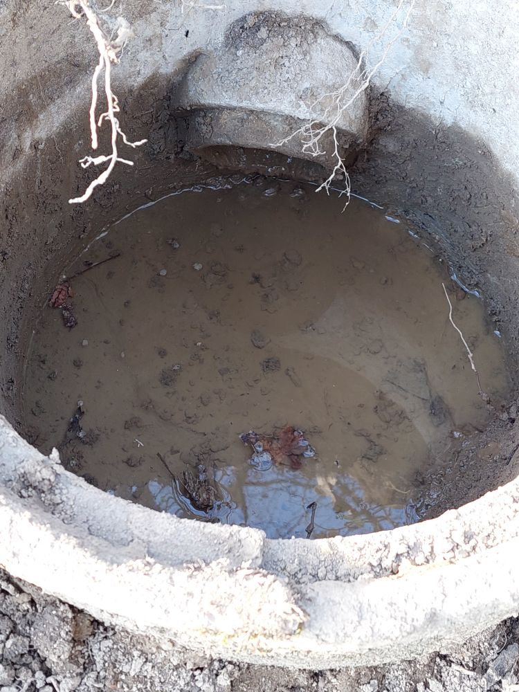 Eine kleiner Entwässerungsschacht, jetzt ohne Schlamm. Auf dem Boden steht etwas Wasser und das Zuflussrohr ist frei.