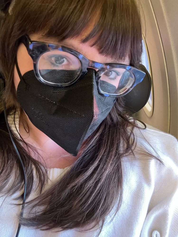 selfie of user snicker-snee sitting in an airplane with a black mask and headphones on 