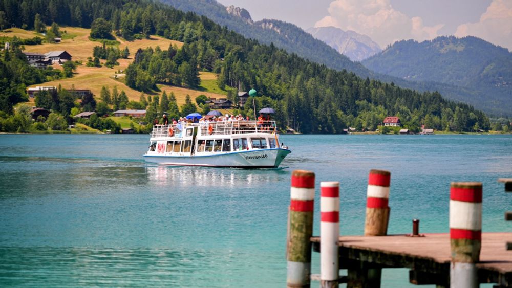 Ausflugsschiff am See
im Hintergrund gegenüberliegendes Ufer
Berge, Himmel
vorne rechts, Anlegesteg mit rot-weiss-roten Pfählen