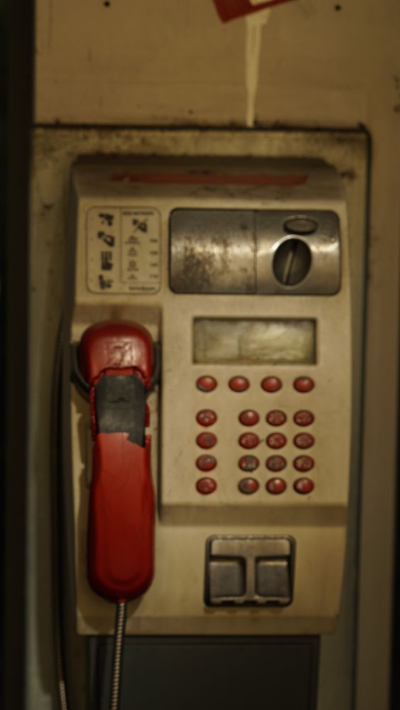 alter Telefonapparat in einer Telefonzelle (lost places) der rote Telefonhörer ist links vom Tastenfeld eingehängt irgendwer hat den Hörer noch mit grauem Isolierband 