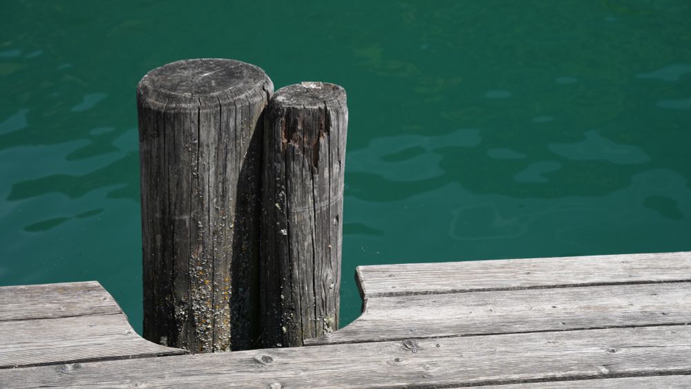 Holzsteg mit Pfählen vor türkisem Seewasser