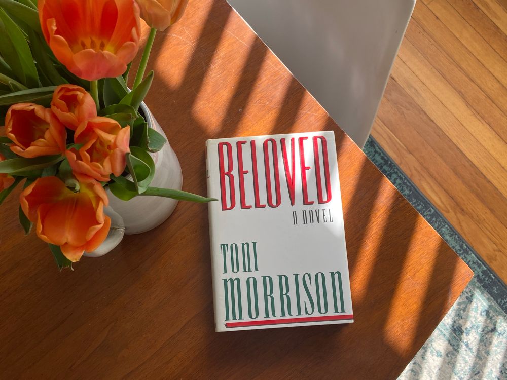 tulips and the novel beloved by toni morrison on a wood tabletop with sun striping across part of the book
