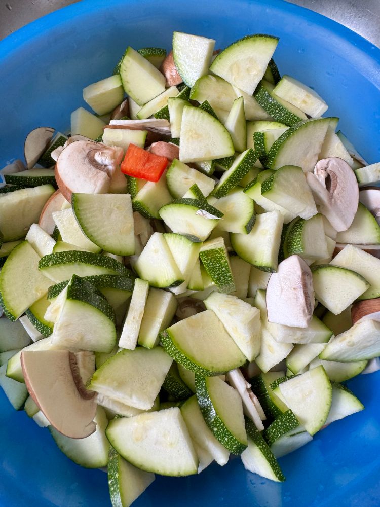 Eine Schüssel mit geschnittenen Zucchini, Champignons und Paprika.
