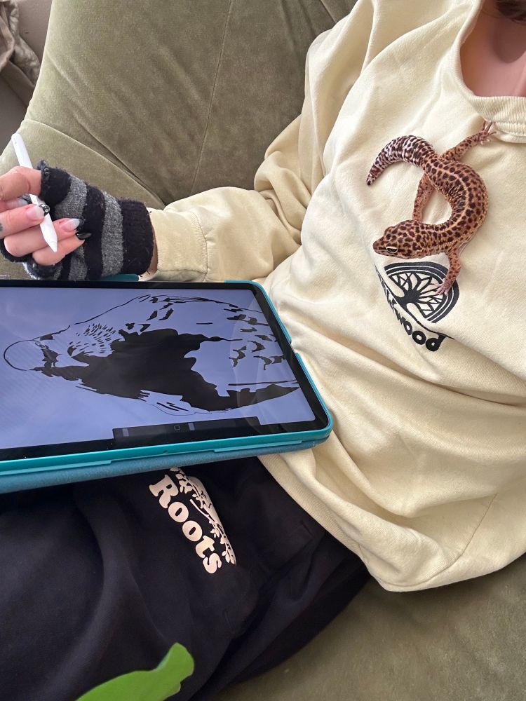 woman sitting with ipad drawing a pigeon with a leopard gecko sitting on her chest. 