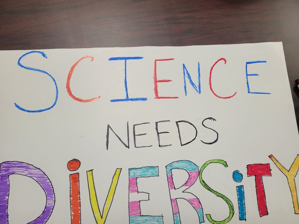 A poster that reads "Science Needs Diversity" and the "ER" in diversity are colored to represent the trans flag