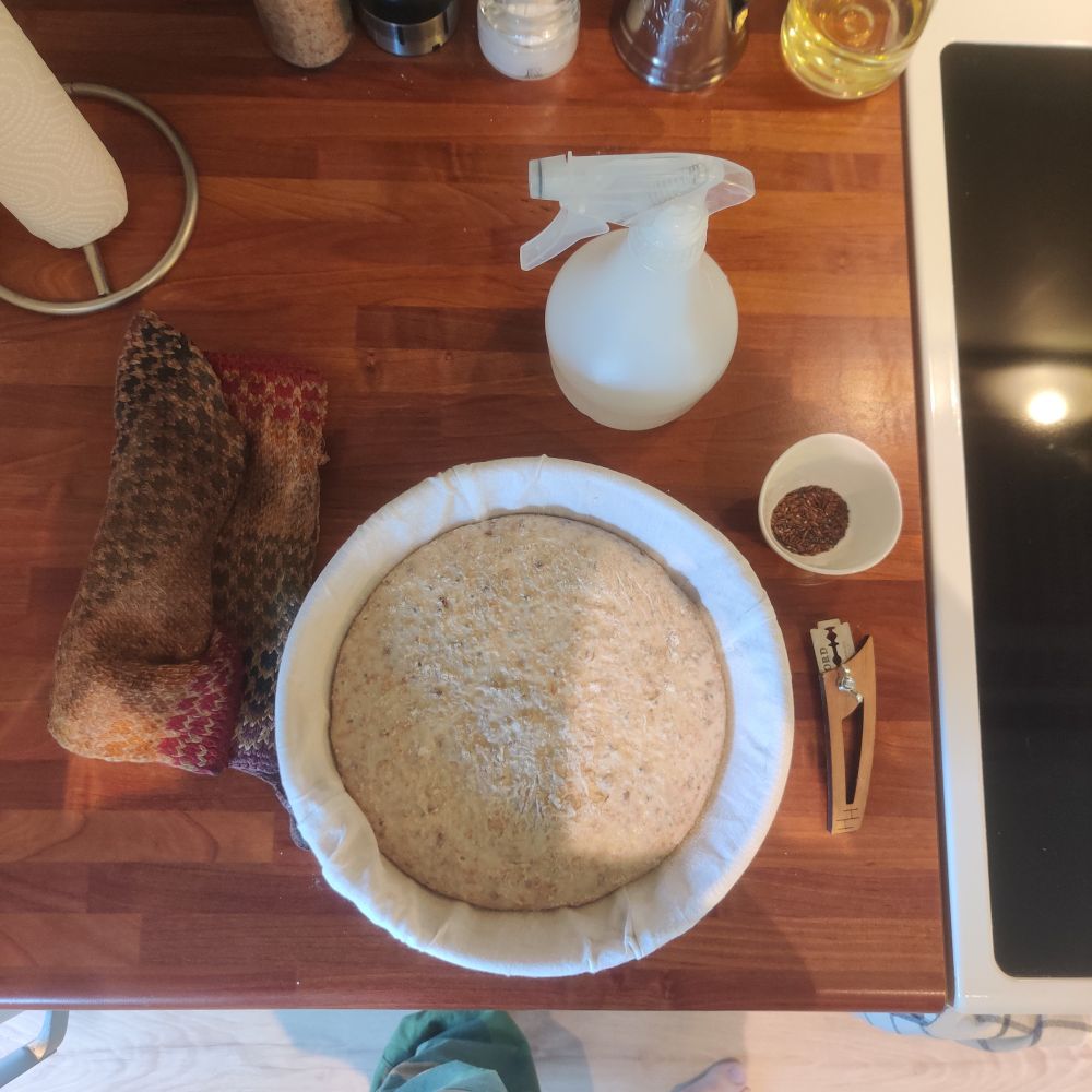 Mise en place for brødbaking. Brød, kniv, lin- og chiafrø og ei spruteflaske.