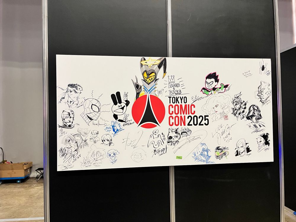 tokyo comiccon 2025と中央に書かれた白いボードにアーティストアレイに参加した作家のサインとアメコミや映画のキャラクターのイラストが寄せ書きされている