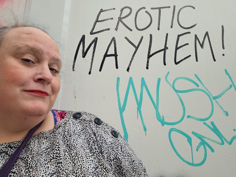 Your humble poster trying to look as sardonic as she can after a knackering walk across town, while stood next to a graffito offering EROTIC MAYHEM!