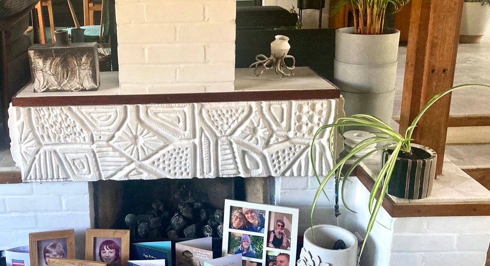 The pot in situ aside a white brick chimney breast surrounded by a 3-D aztec (?) style frieze, again painted white. Also in frame are a sad looking spider plant, that used to be Alice’s. She did not take good care of it. It looks healthier than it used to but it’s struggling. On the other side of the chimney breast is a pot I bought in Norwich where I went to complete the final draft of Her Name is Alice. On the hearth are family photos and birthday and anniversary cards. 