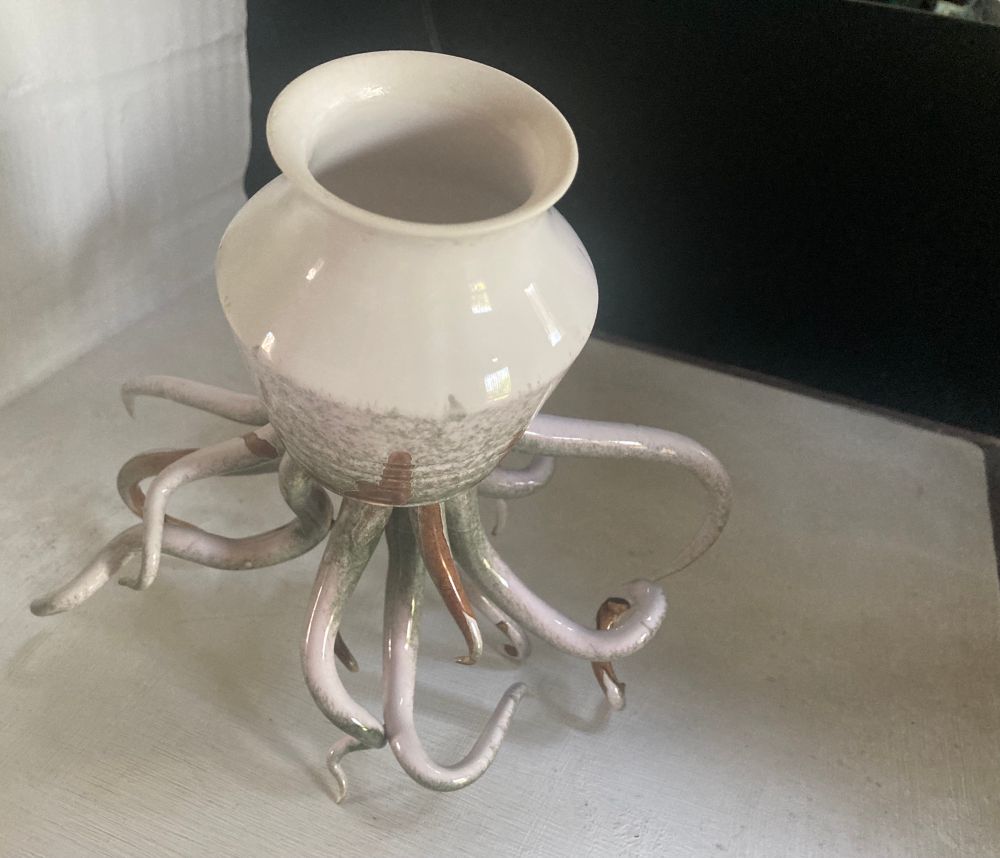 A ceramic pot in stone/ cream/ grey/ brown colour way.

The pot sits askew a myriad of tentacles, fifteen I think.