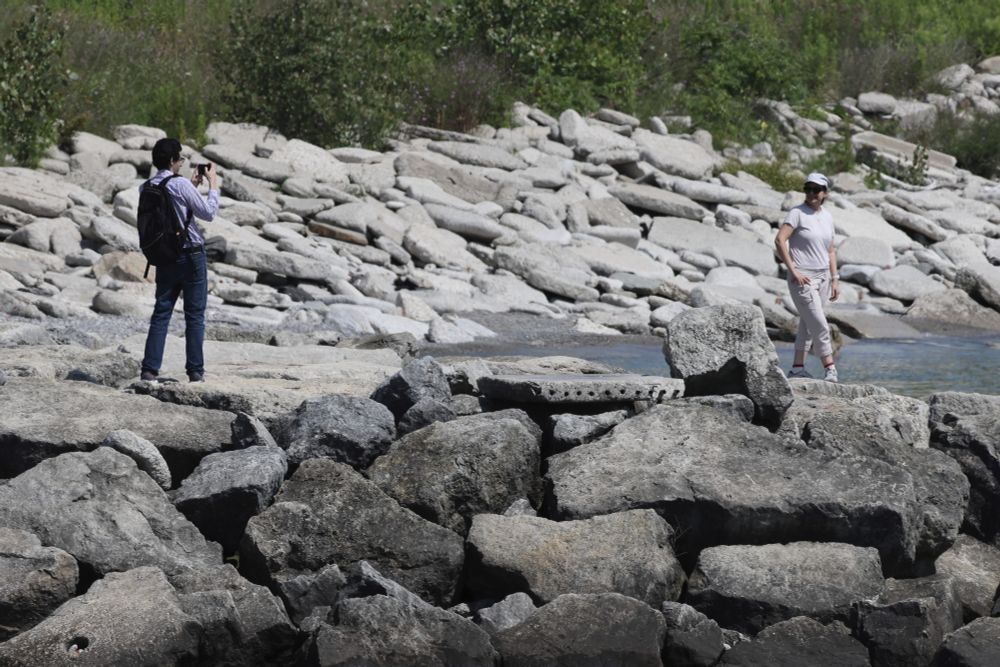 A man taking a photo of his partner on a rocky shoreline.