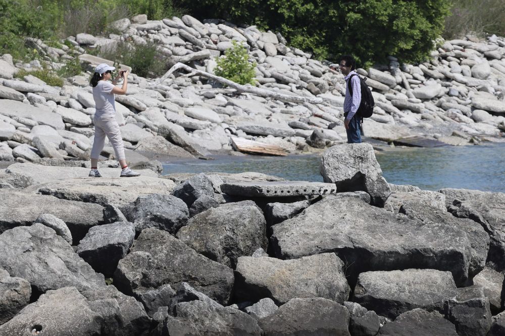 A woman taking a photo of her partner on a rocky shoreline.