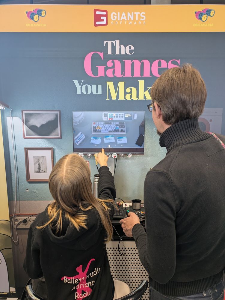 a young girl pointing at a screen, playing a video game and showing the level to another player.