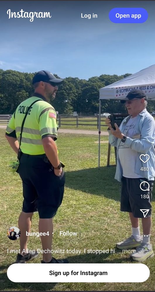 Screenshot of a dorky-ass Alan Dershowitz talking to a West Tisbury police officer at a farmers' market. Dershowitz is recording the interaction with his phone.