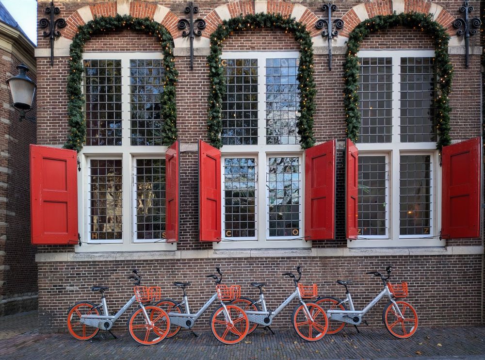 4 oranje fietsen staan onder de glas in lood ramen met open rode luiken
van een middeleeuws pand in Gouda. Kerstversiering met brandende lichtjes rondom de ramen. 
