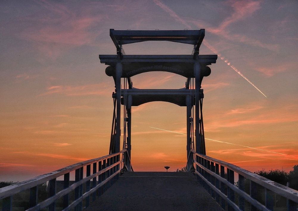 Ophaalbrug vanaf laag punt in het midden genomen. Tijdens een oranje zonsopkomst met hier en daar fellere oranje vegen en condens strepen.
