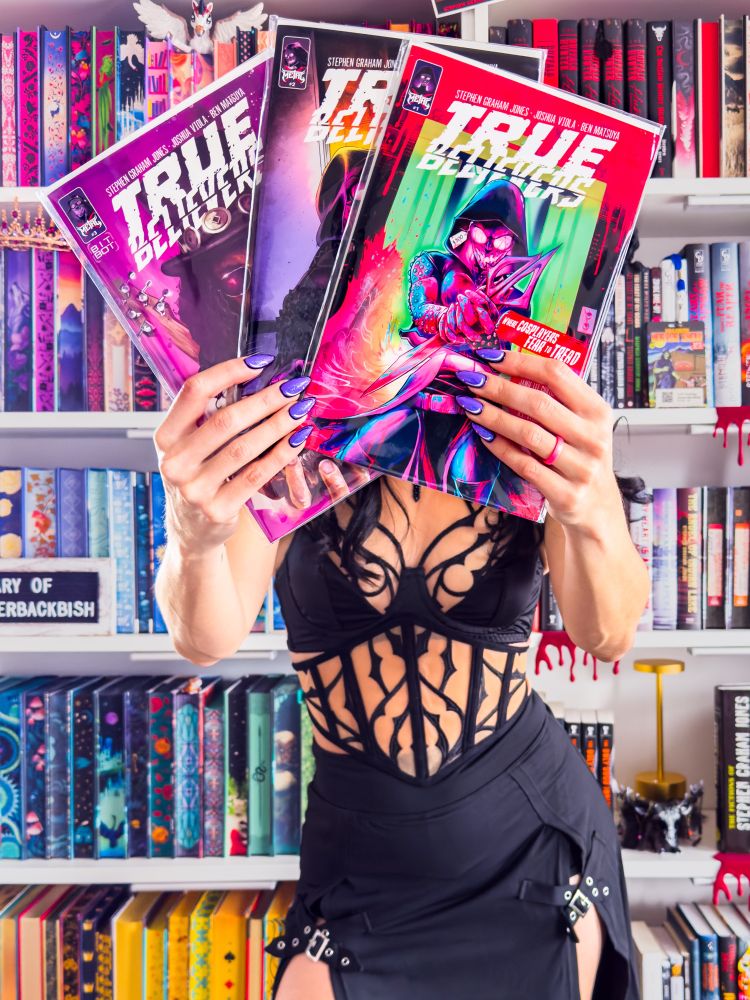 Three True Believes comic books held up by a glittery purple pop art manicure 