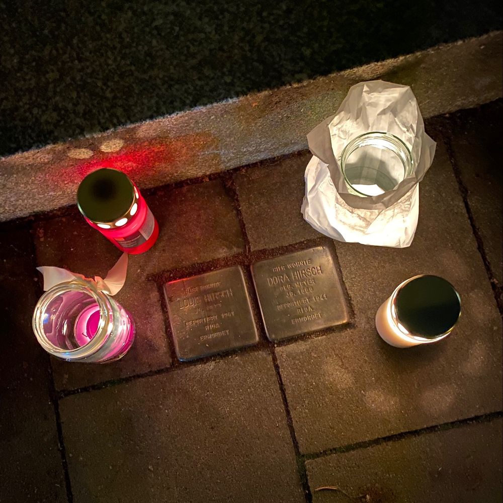 Foto von zwei Stolpersteinen von Dora Hirsch und Louis Hirsch, um die vier Lichter stehen.