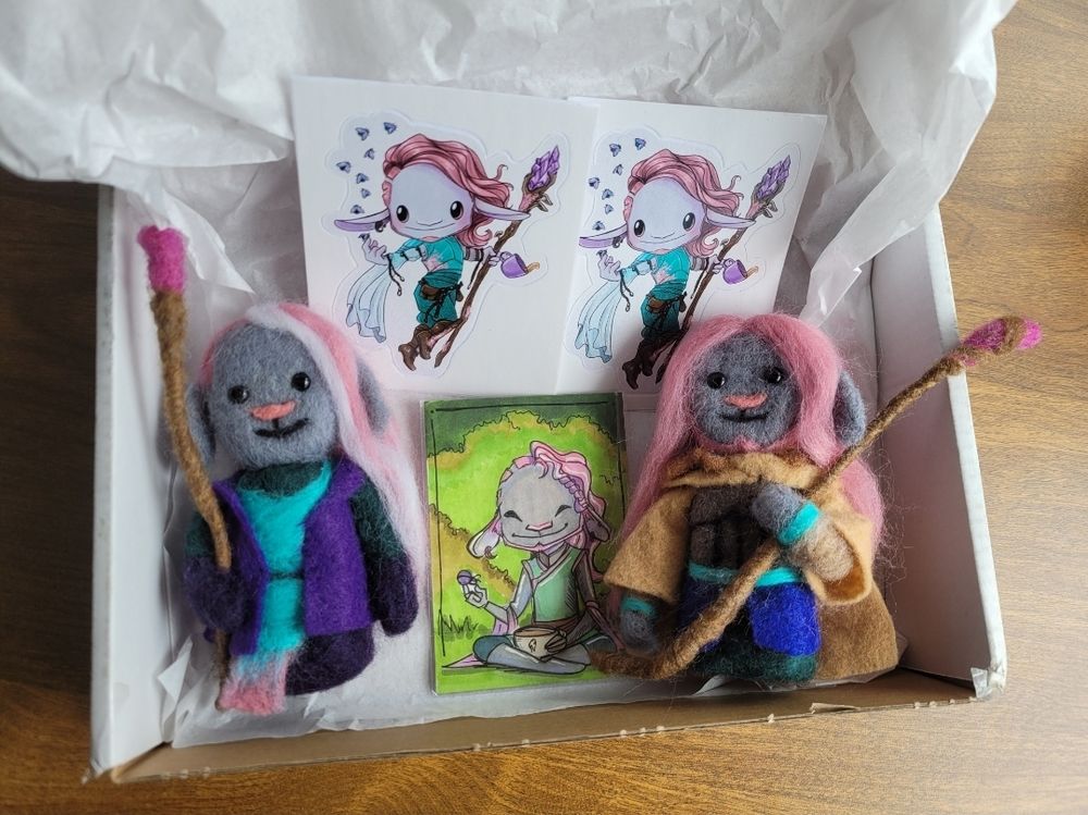 Level 10 and level 20 Caduceus beans with two Caduceus stickers and a chibi Caduceus drawing laying in the box they arrived in. 