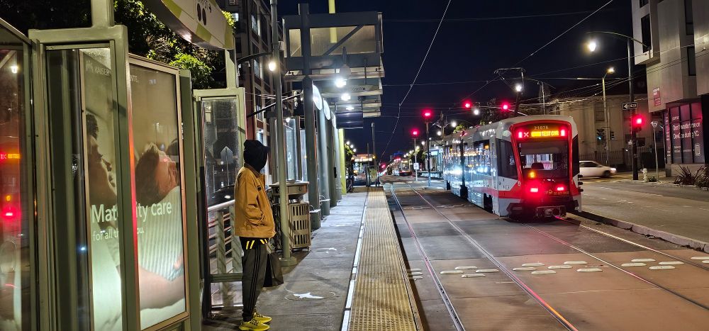 Two different generation light rail vehicles meet in a transit median, and a bus joins the party.