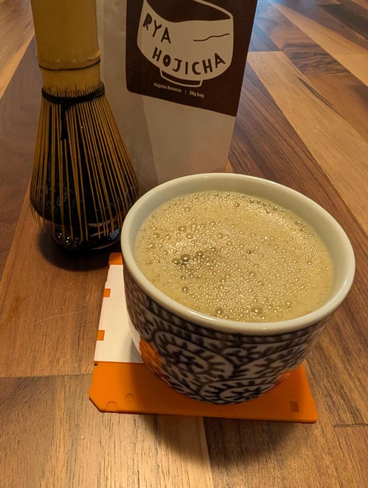 A cup of hojicha matcha on a black walnut tabletop with whisk