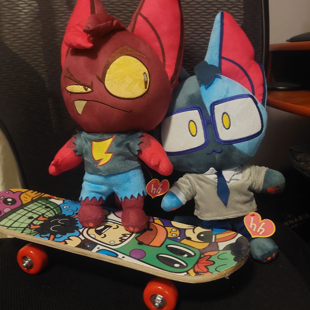 plushies of mars (red cat on left) and achilles (blue cat on right). characters from batshaped's Hello From Halo Head. mars is riding a cute skateboard i bought for 14$ and this exact purpose, achilles is standing next to her (happy to be here).