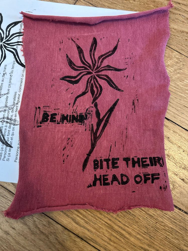 A lino print on a red fabric. It's a prickly flower. On each side of its stem is written: "Be kind. Bite their head off."