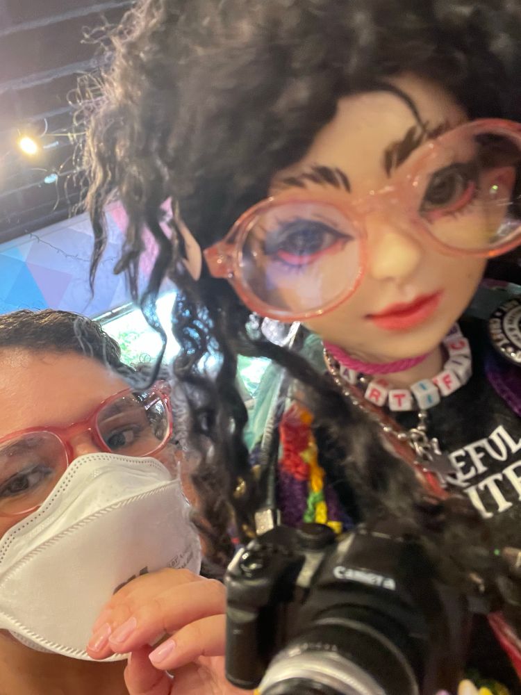 A close up a ball jointed doll that is 1/4 scale, it us dressed to look like a smaller version of the person in the background.