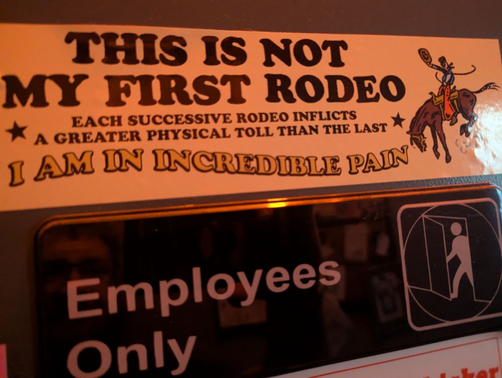A picture of a sticker on a door that reads "This is not my first rodeo. Each successive rodeo inflicts a greater physical toll than the last. I am in incredible pain."
