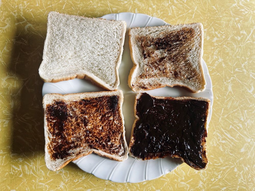 Four slices of bread arranged on a plate with varying amounts of Vegemite spread on each piece, ranging from 'none' to 'ridiculous'