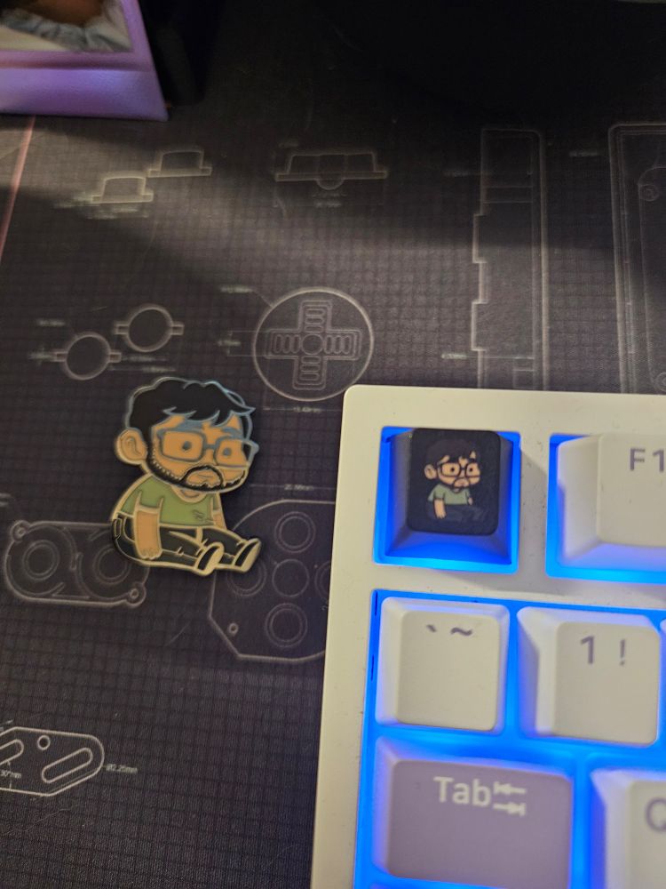 A small Puerto Rican man sits contentedly, in pin and key cap form!