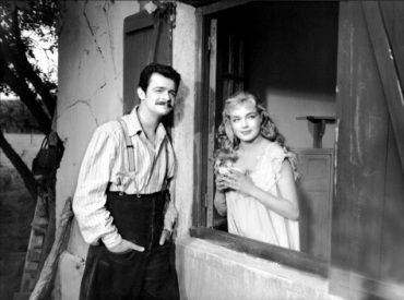 Jo Manda (Serge Reggiani) stands outside a large window in the rustic home he shares with Marie (Simone Signoret) who is looking out that window on the right, in a nightgown and holding a bowl. This is during an idyllic period when they are living in the country together, but trouble is waiting for them. 