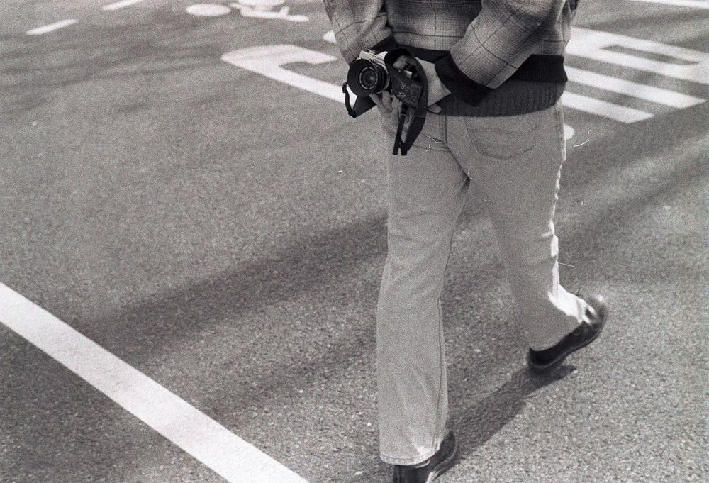 Un monsieur pris en photo de dos, se balade avec un appareil photo dans le dos 