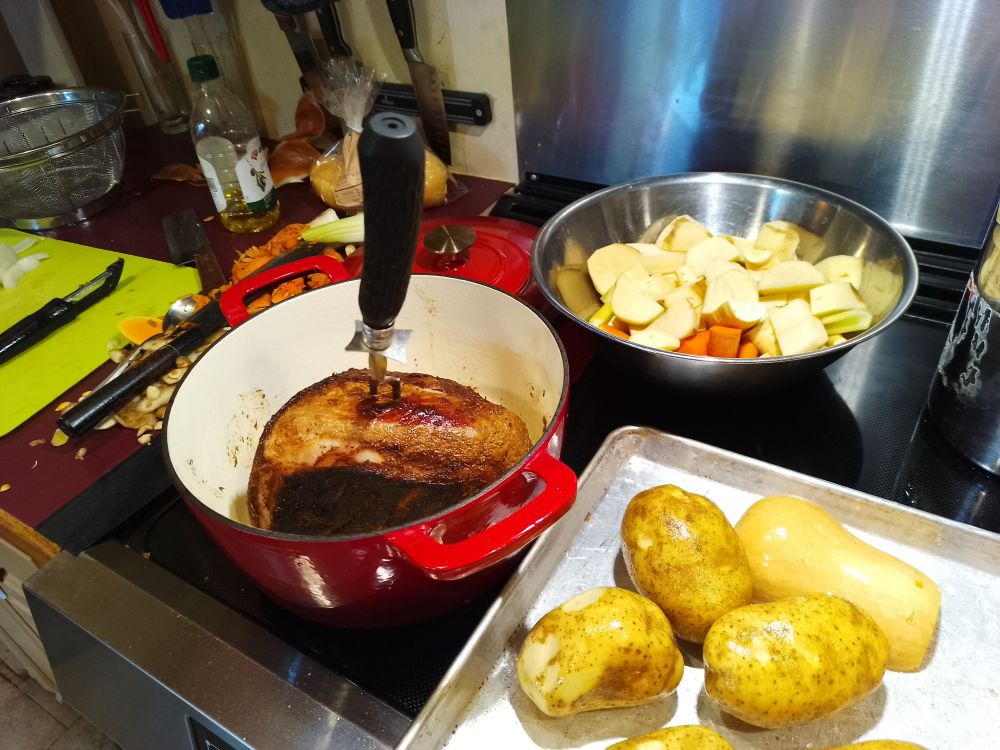 Sheet pan of squash and whole oiled potatoes, bowl full of mixed chopped root veg and celery, big Dutch oven pot with a roast in it getting a crust, a big fork is sticking out of the meat