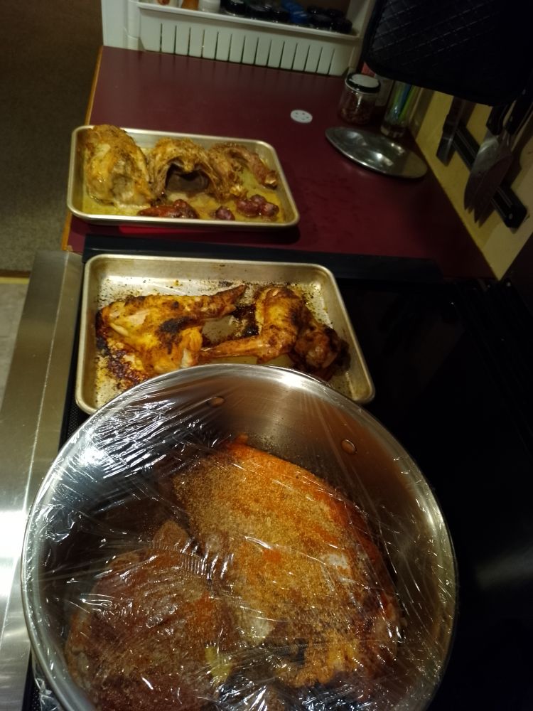 Two pans of roasted turkey bits and a plastic covered pot witbh herb covered turkey meat