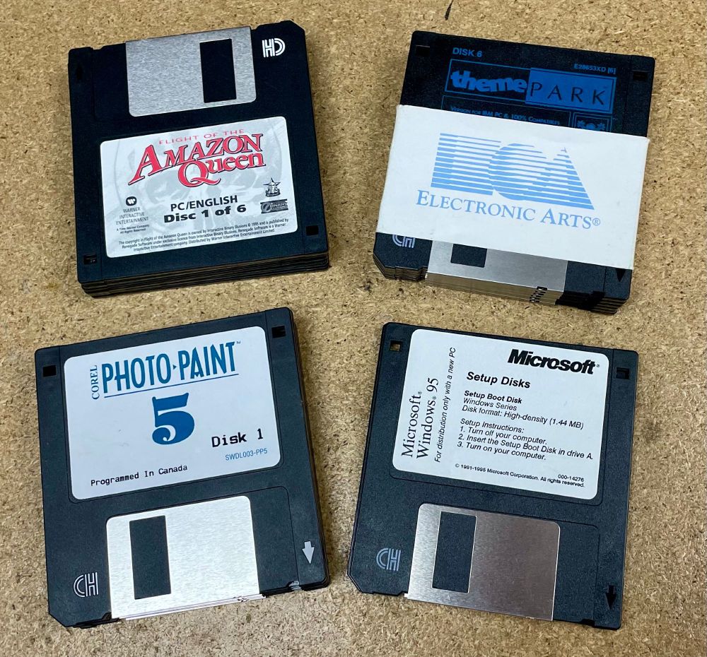 “Four vintage 3.5-inch floppy disks displayed on a wooden surface. The disks include ‘Flight of the Amazon Queen’ (Disc 1 of 6), ‘Theme Park’ by Electronic Arts, ‘Corel Photo-Paint 5’ (Disk 1), and ‘Microsoft Windows 95 Setup Disk’ (Setup Boot Disk).”